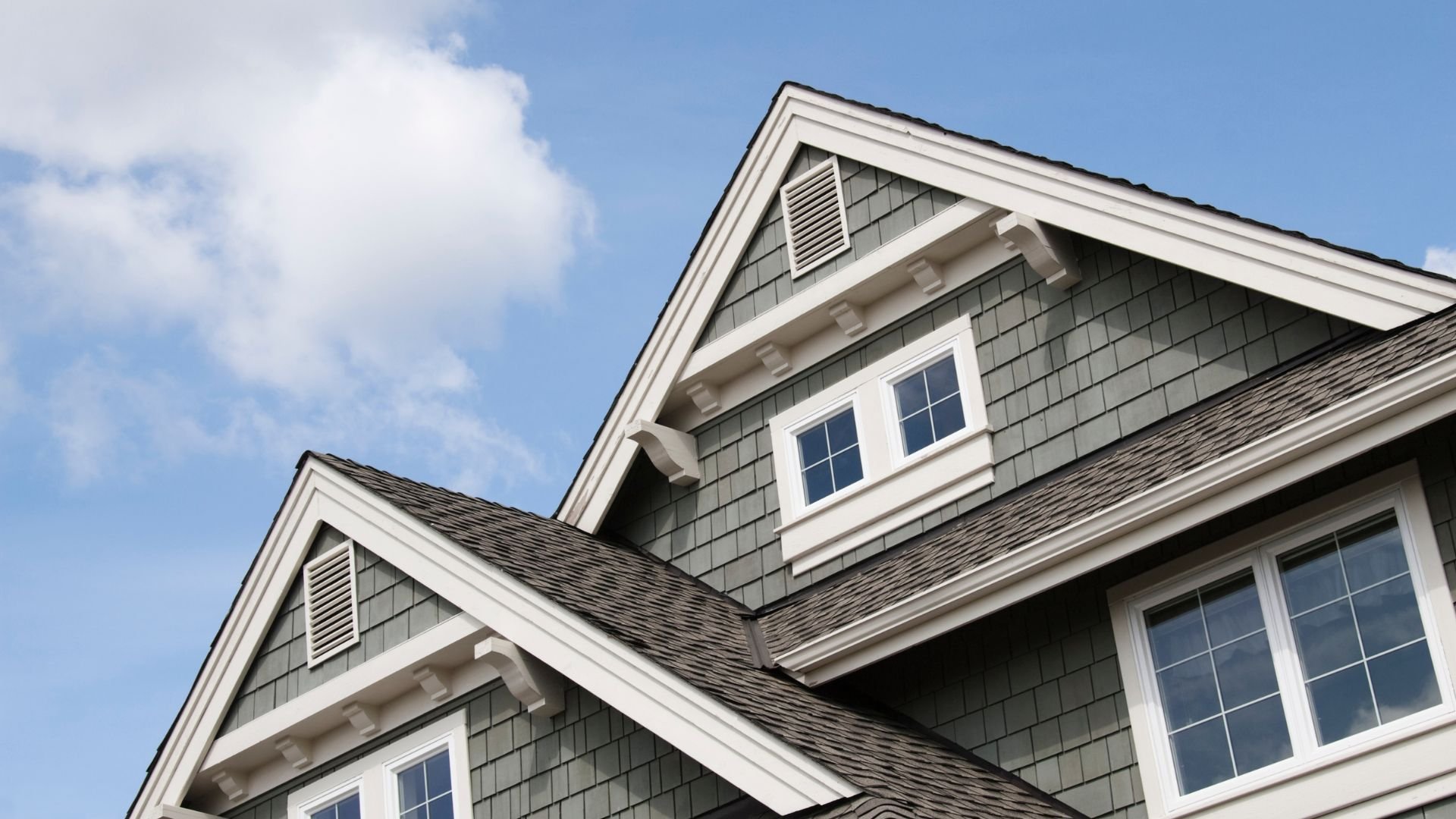 Gray shingled house with white trim and windows against blue sky