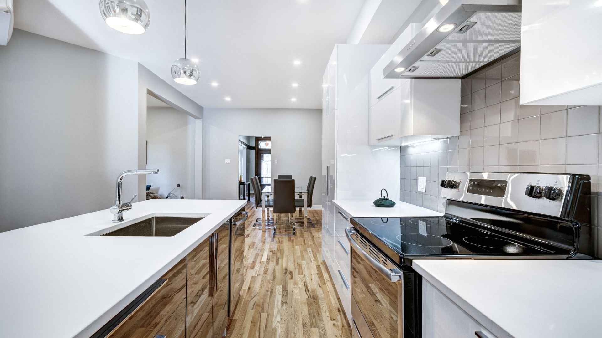 Modern kitchen with white counters, wooden floor, and stainless steel appliances